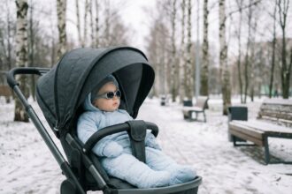 Bébé en poussette tout-terrain portant des lunettes de soleil UV pour nourrisson lors d'une balade hivernale dans un parc enneigé
