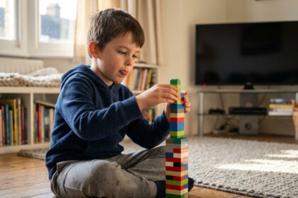 Enfant concentré jouant avec des LEGO sur le sol d'un salon, la télévision éteinte en arrière-plan